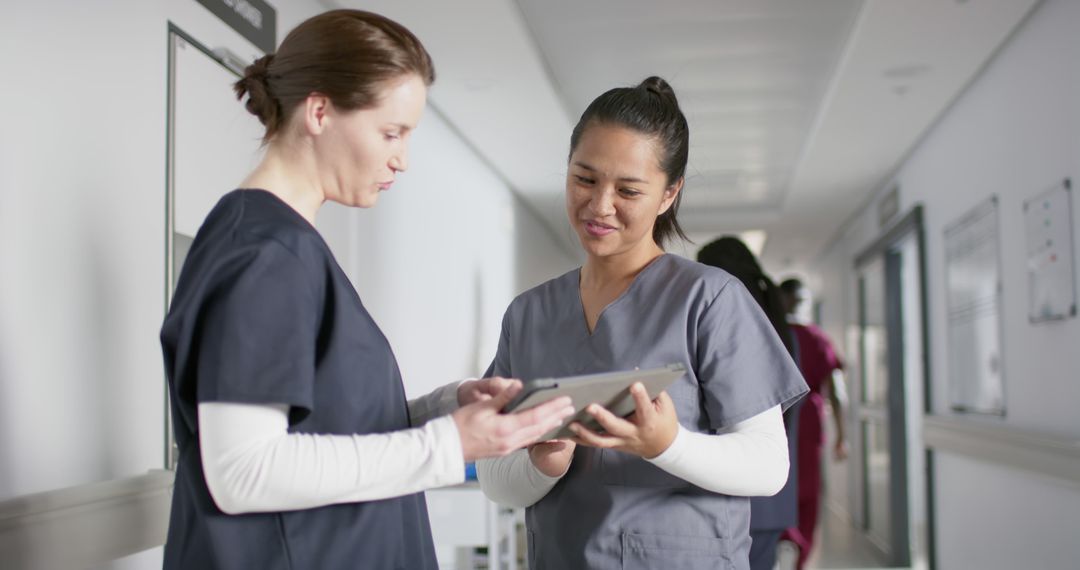 Two Nurses in Hospital Corridor Discussing Medical Records - Free Images, Stock Photos and Pictures on Pikwizard.com