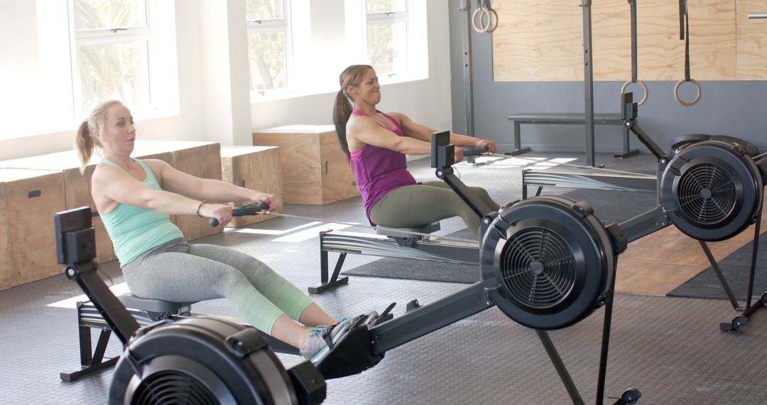 Two Women Exercising on Rowing Machines in Bright Gym - Free Images, Stock Photos and Pictures on Pikwizard.com