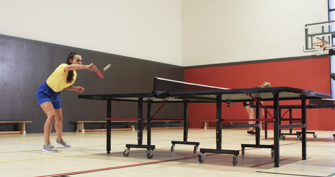 Two Women Energetically Playing Table Tennis in Gymnasium