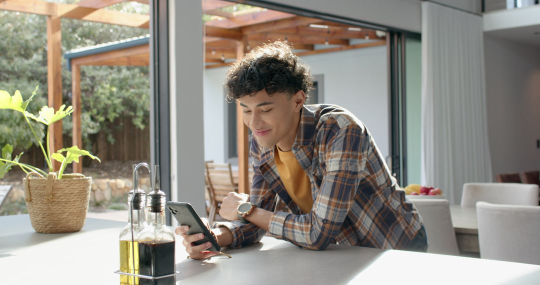 Young Man Using Smartphone in Modern Kitchen with Sunlight