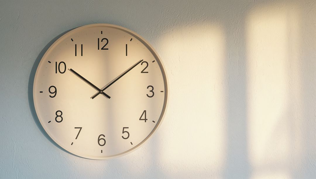 Minimal round wall clock casting window-grid shadow in warm morning sunlight