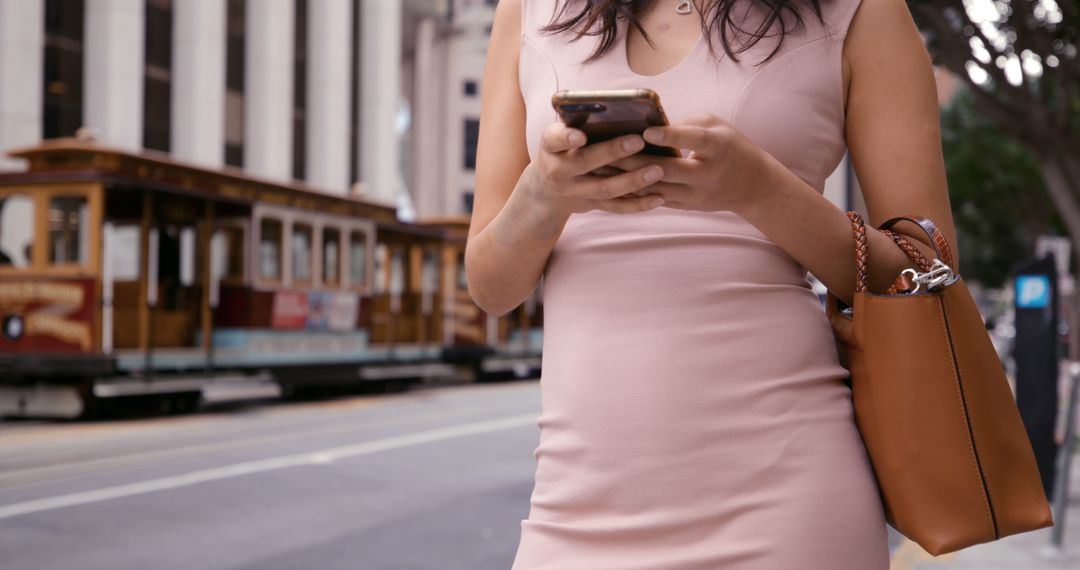 Woman using smartphone on city street with tram in background - Free Images, Stock Photos and Pictures on Pikwizard.com