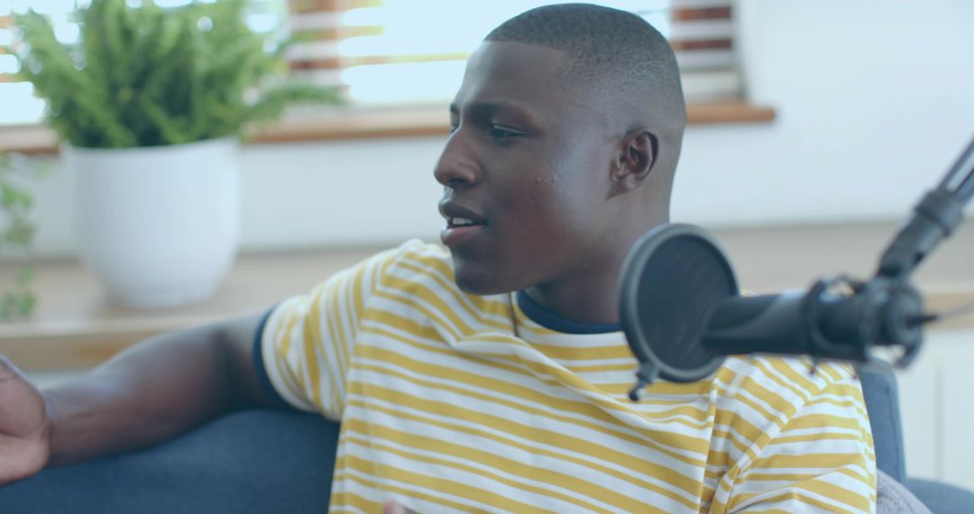 Young man recording podcast on couch with professional microphone and natural daylight