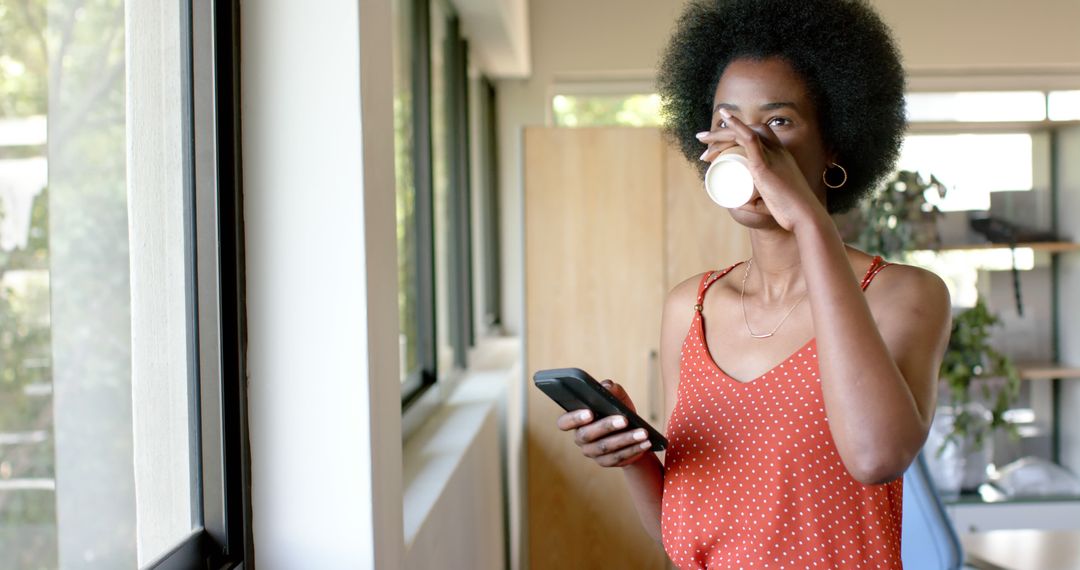 Young Black Woman Drinking Coffee and Using Smartphone in Office - Free Images, Stock Photos and Pictures on Pikwizard.com