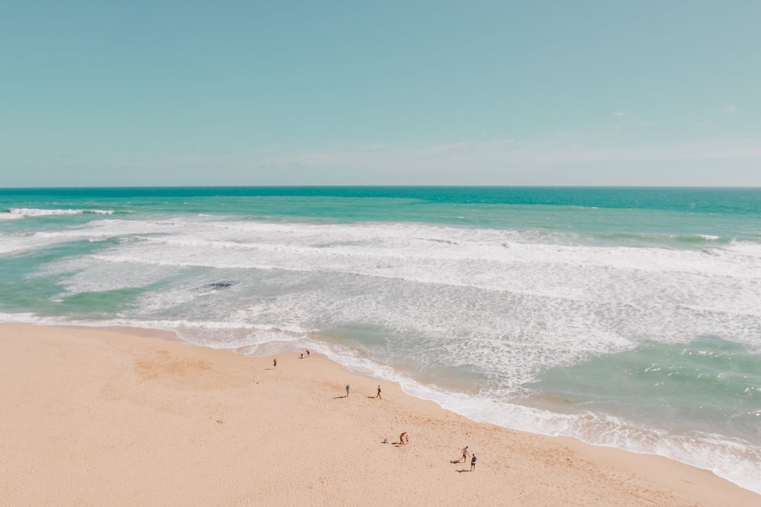 Sunlit turquoise waves rolling toward wide sandy beach with distant walkers