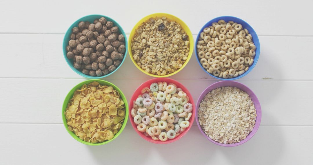 Colorful Bowls Displaying Assorted Breakfast Cereals in Neat Grid on White Wooden Tabletop