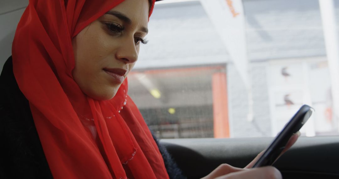 Focused Woman in Red Hijab Using Smartphone in Car - Free Images, Stock Photos and Pictures on Pikwizard.com