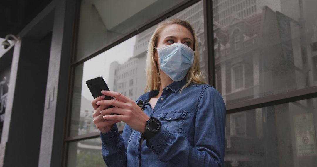 Young Woman in Denim Using Smartphone Wearing Protective Face Mask Outdoors - Free Images, Stock Photos and Pictures on Pikwizard.com