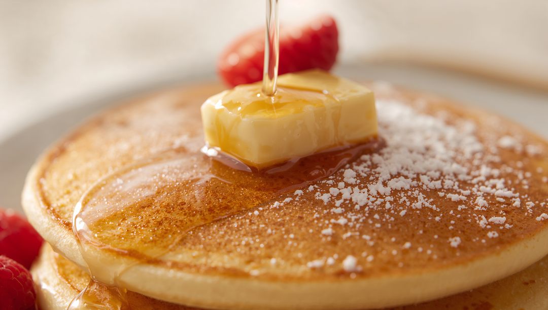 Golden Pancake Stack Drizzling Maple Syrup with Melting Butter, Powdered Sugar, Fresh Raspberries