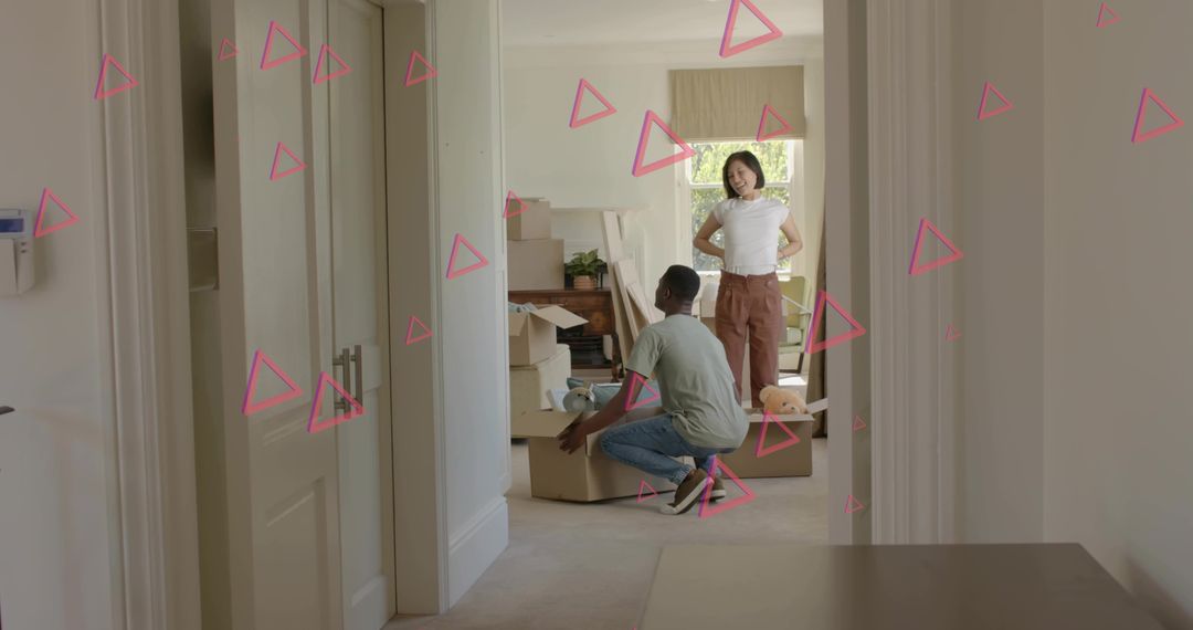 Two Adults Unpacking Boxes in Daylit Hallway with Pink Triangle Overlays Showing Teamwork