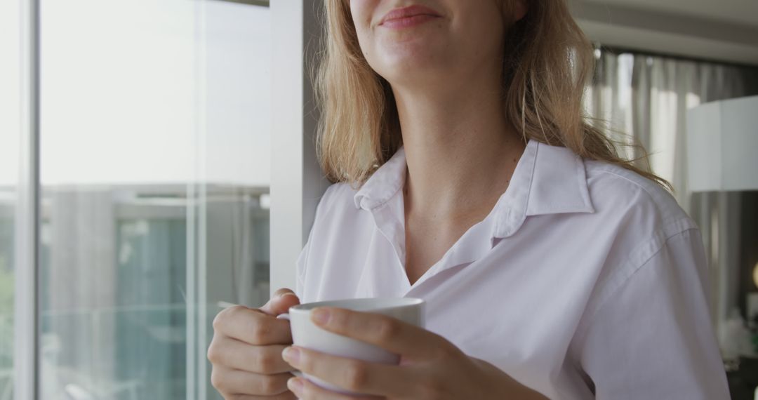 Happy caucasian woman wearing white shirt and drinking coffee in modern apartment - Free Images, Stock Photos and Pictures on Pikwizard.com
