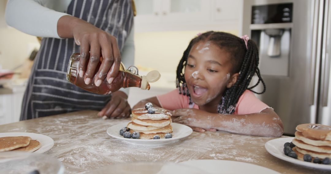 Excited Young Girl Watching Pancakes Being Topped with Syrup in Kitchen - Free Images, Stock Photos and Pictures on Pikwizard.com