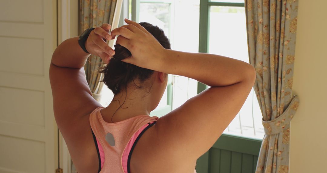 Woman Preparing for Workout Pulling Hair Back Near Window - Free Images, Stock Photos and Pictures on Pikwizard.com