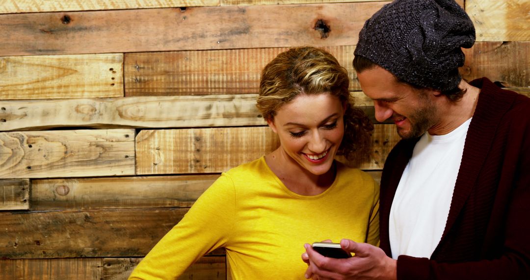 Happy Couple Sharing Smartphone Moment Against Wooden Wall - Free Images, Stock Photos and Pictures on Pikwizard.com