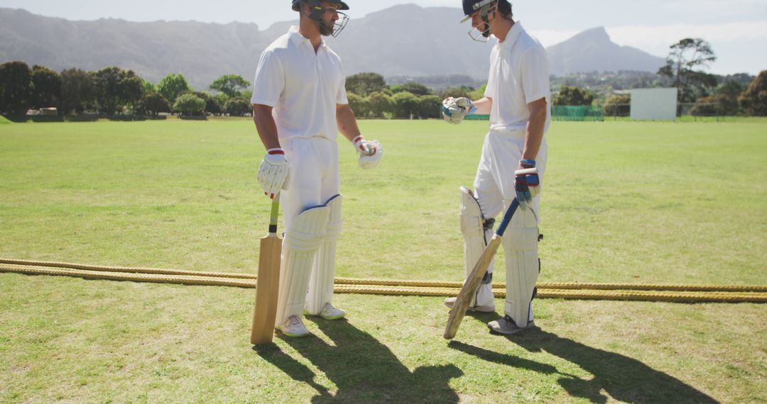 Cricket Players in White Uniforms Preparing for Game on Sunny Field - Free Images, Stock Photos and Pictures on Pikwizard.com