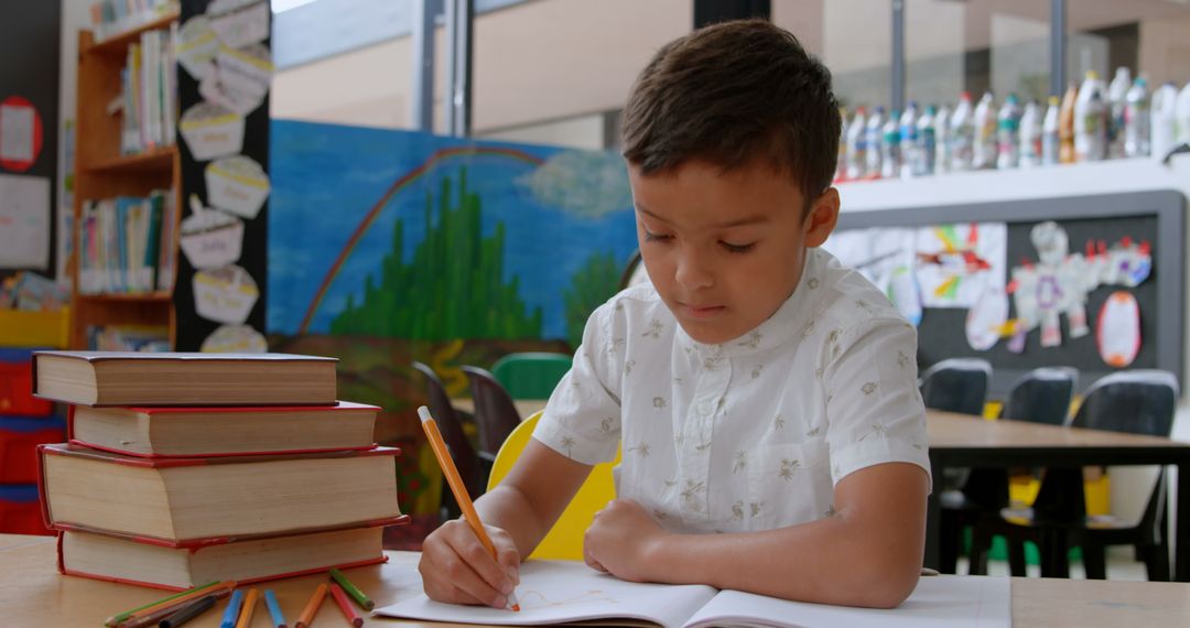 Focused Schoolboy Writing in Classroom with Books and Pencils