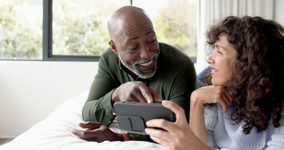 Joyful Mature Couple Sharing Phone Experiences in Bedroom
