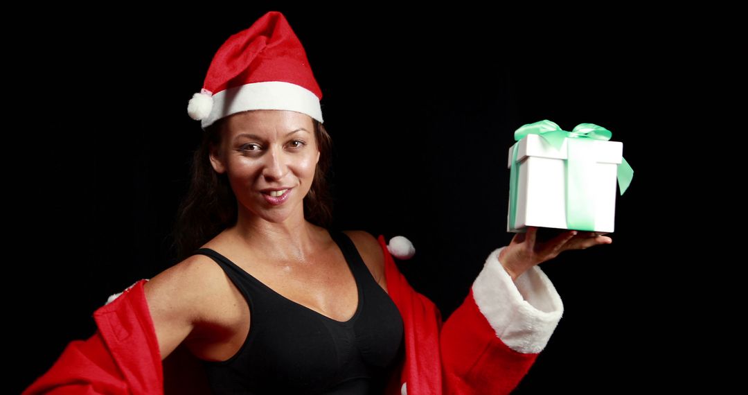 Joyful Woman Holding Christmas Gift in Santa Hat and Red Coat - Free Images, Stock Photos and Pictures on Pikwizard.com