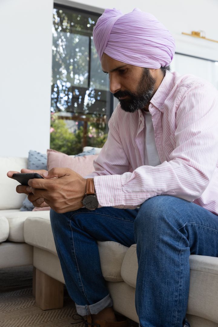 Man Wearing Lavender Turban Using Smartphone on Sofa at Home