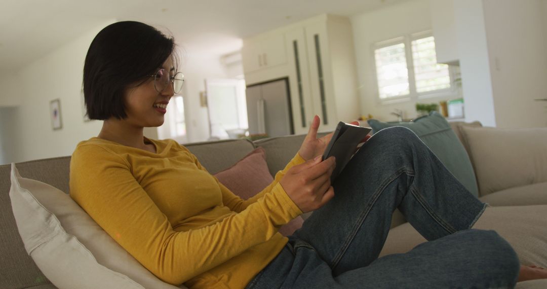 Young Woman Smiling and Using Tablet While Relaxing on Sofa - Free Images, Stock Photos and Pictures on Pikwizard.com