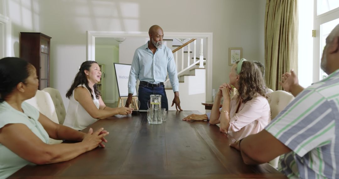 Senior Man Leading Group Meeting at Home Around Wooden Table