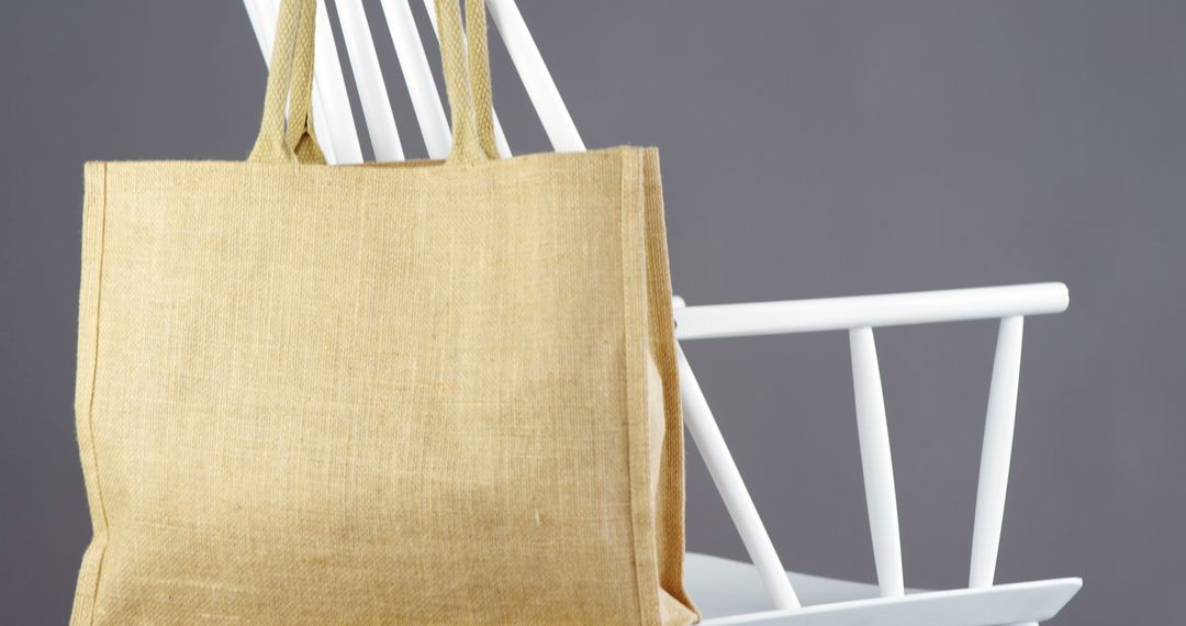 A beige tote bag hangs on the back of a white chair, with copy space - Free Images, Stock Photos and Pictures on Pikwizard.com