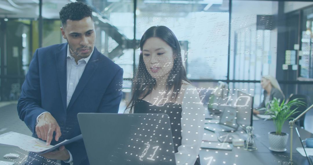 Collaborating over data on laptop in modern open plan office with glass walls and charts