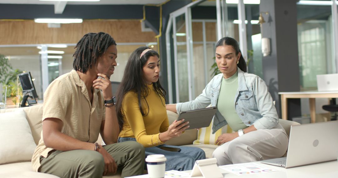 Diverse team collaborating over tablet and laptop, reviewing charts in modern coworking lounge