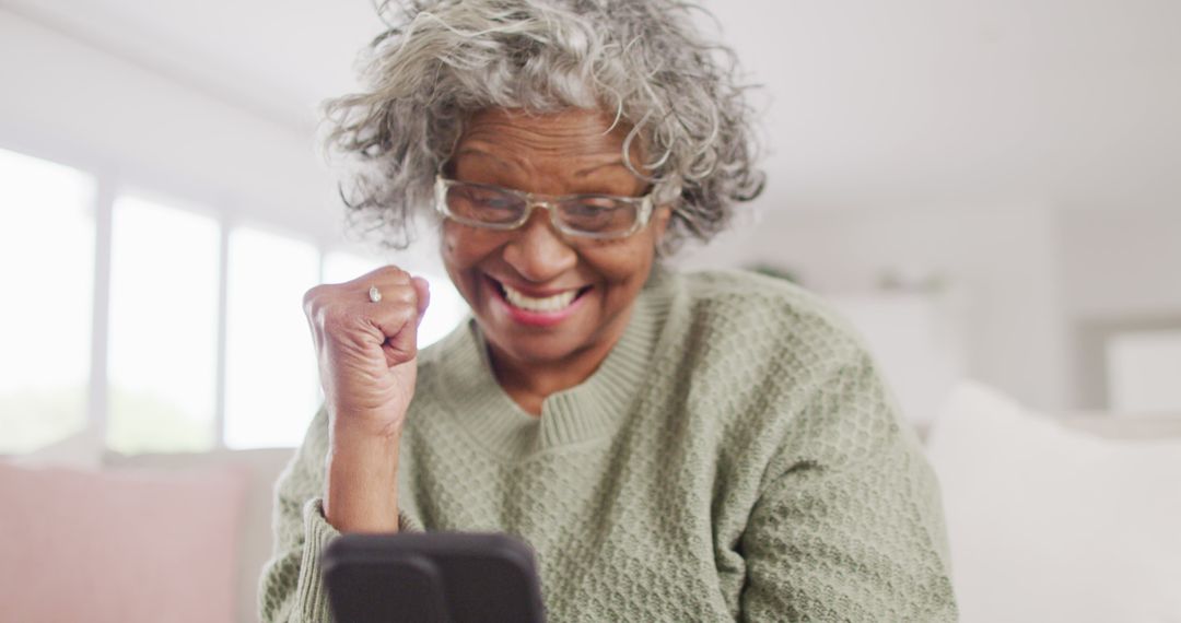 Elderly Woman Celebrating Good News on Smartphone at Home - Free Images, Stock Photos and Pictures on Pikwizard.com