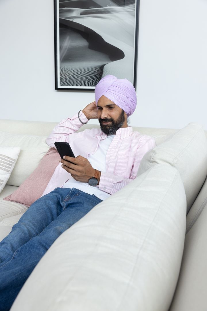 Indian Man Relaxing On Sofa Using Smartphone at Home
