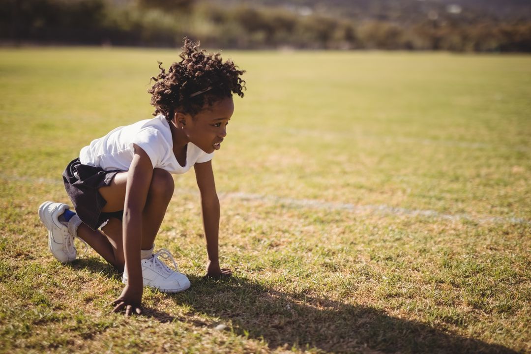 Young Athlete Crouching at Start Line on Green Field