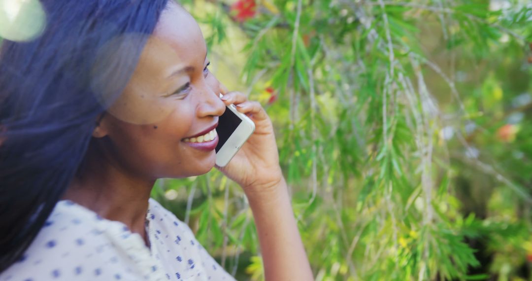 Smiling African American woman talking on smartphone outdoors in springtime - Free Images, Stock Photos and Pictures on Pikwizard.com