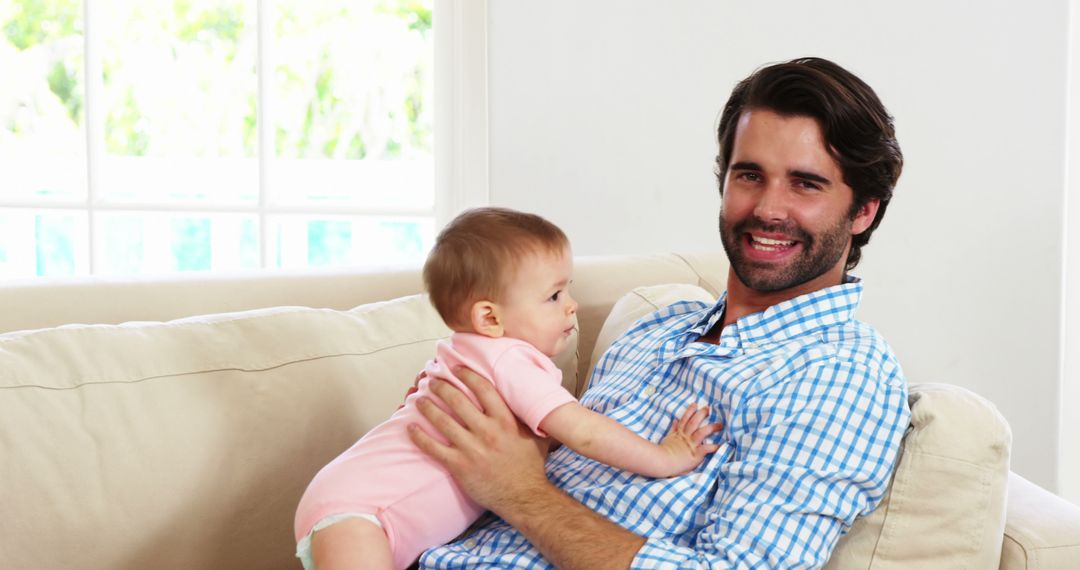 Smiling Father Holding Baby in Bright Living Room - Free Images, Stock Photos and Pictures on Pikwizard.com