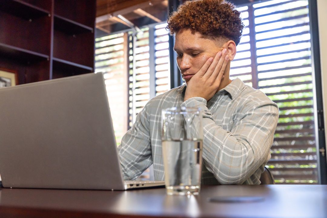 Male Student Pondering While Using Laptop in Home Office Setting