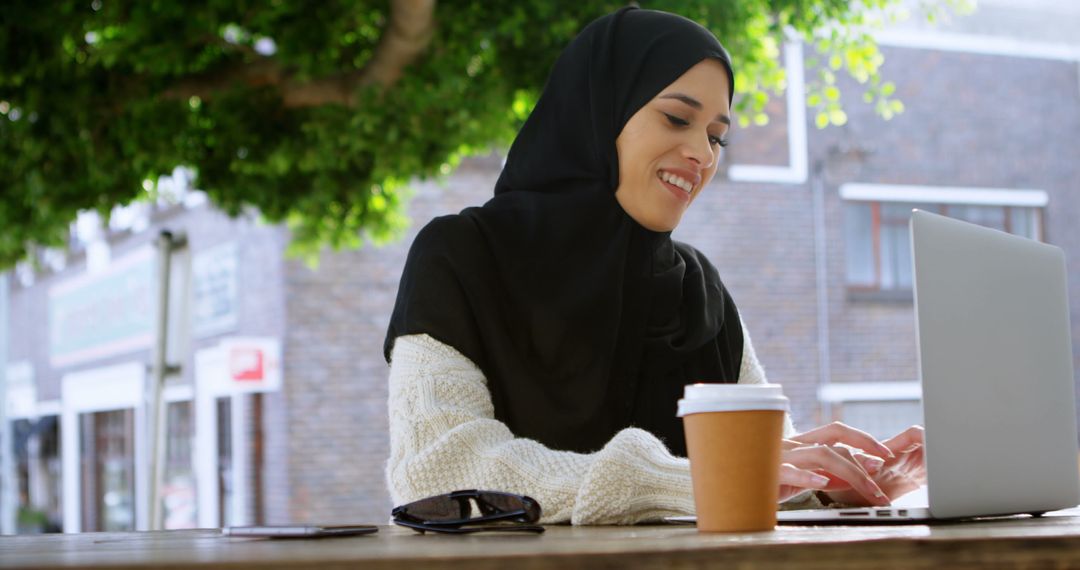 Smiling Woman in Hijab Using Laptop Outdoors at Cafe - Free Images, Stock Photos and Pictures on Pikwizard.com