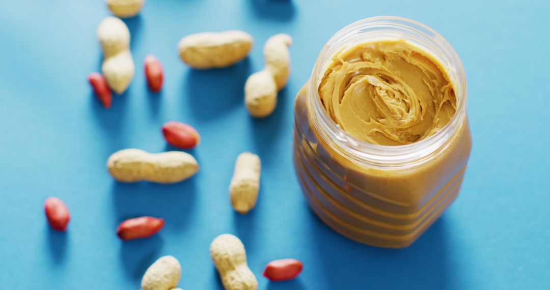 Close Up of Creamy Peanut Butter and Peanuts on Blue Background