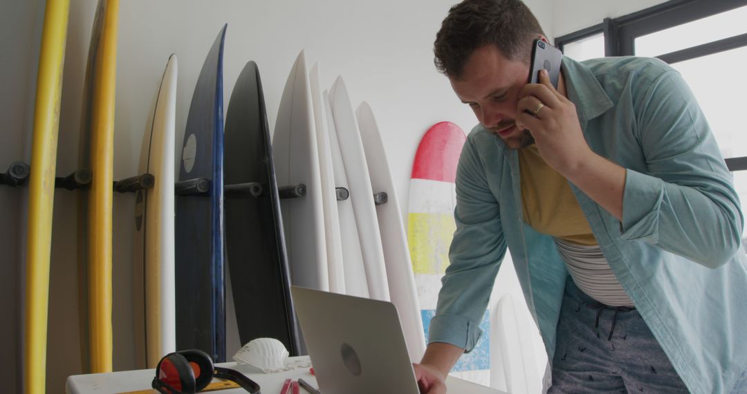 Young Man Managing Surf Shop Business Over Phone and Laptop - Free Images, Stock Photos and Pictures on Pikwizard.com