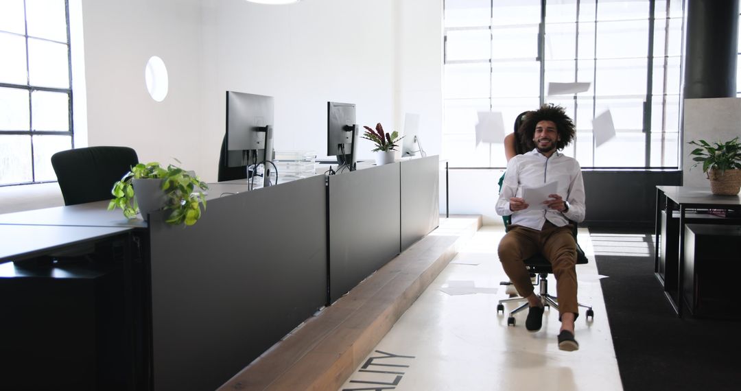 Colleagues Enjoying Office Chair Ride in Modern Workspace