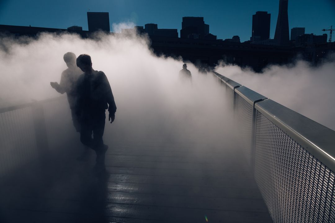 Silhouetted Figures Walking Through Dense Fog on City Bridge - Free Images, Stock Photos and Pictures on Pikwizard.com