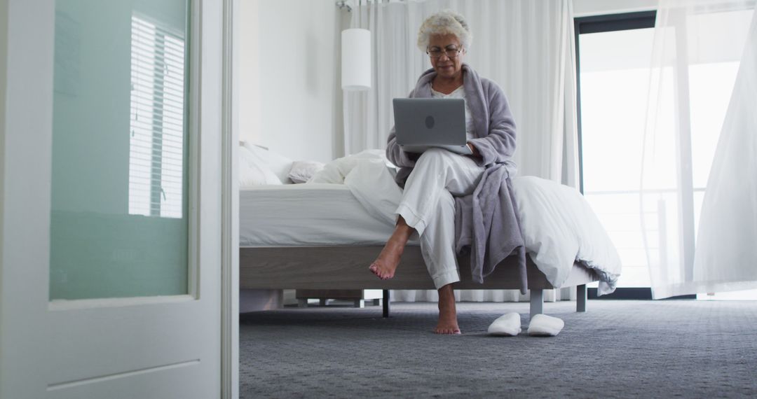 Elderly Woman in Robe Using Laptop on Bed in Minimalist Bedroom - Free Images, Stock Photos and Pictures on Pikwizard.com