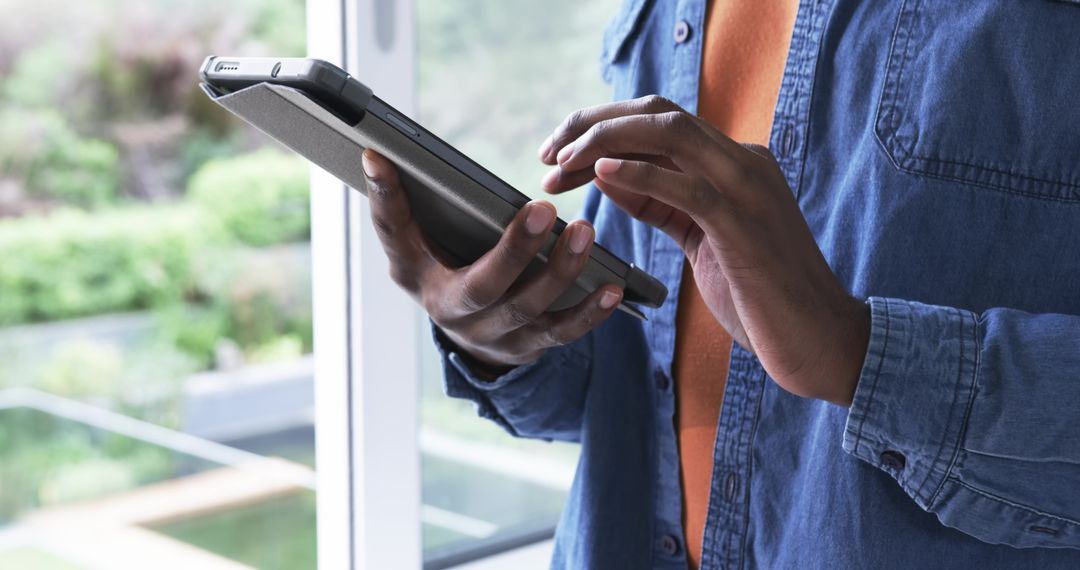 African American man holding tablet folio by window using touchscreen for remote work