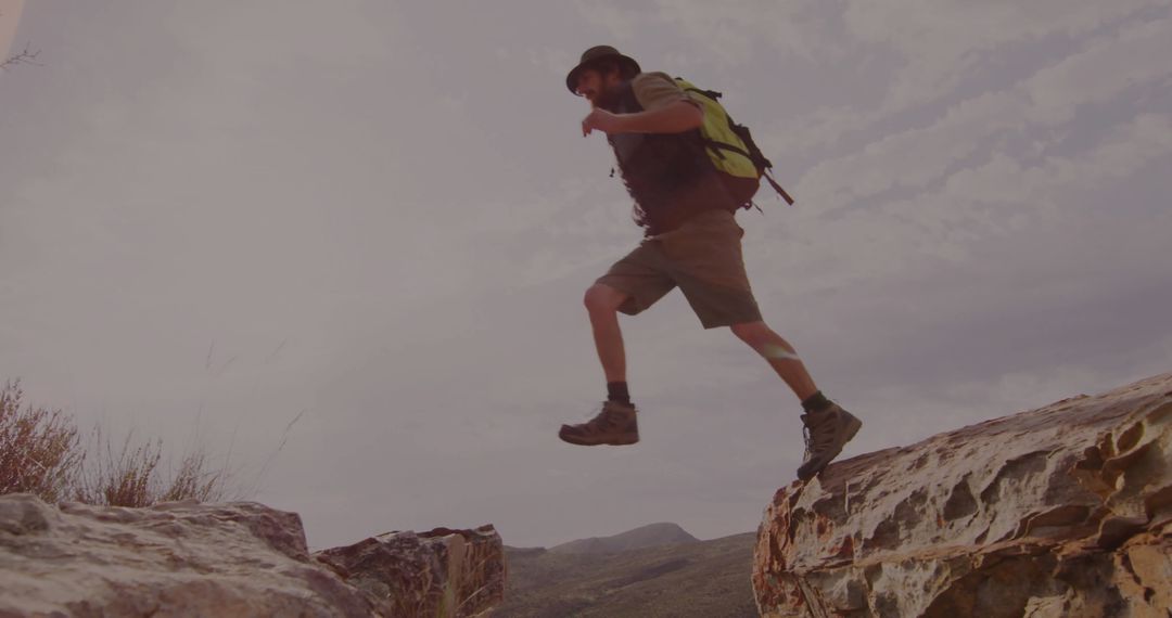Adventurous Hiker Jumping Between Rocky Ledges on Arid Trail