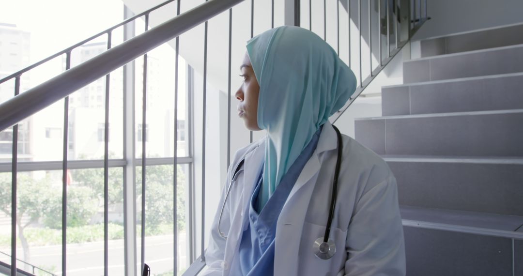 Thoughtful Female Doctor in Hijab Standing on Stairs of Modern Hospital - Free Images, Stock Photos and Pictures on Pikwizard.com