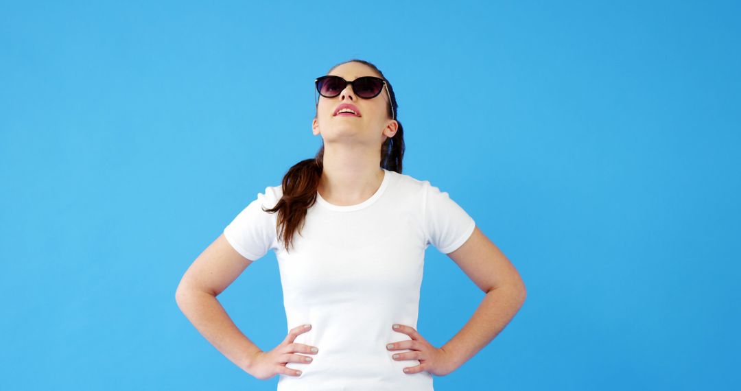 Young Woman Wearing Sunglasses Looking Up Against Blue Background - Free Images, Stock Photos and Pictures on Pikwizard.com