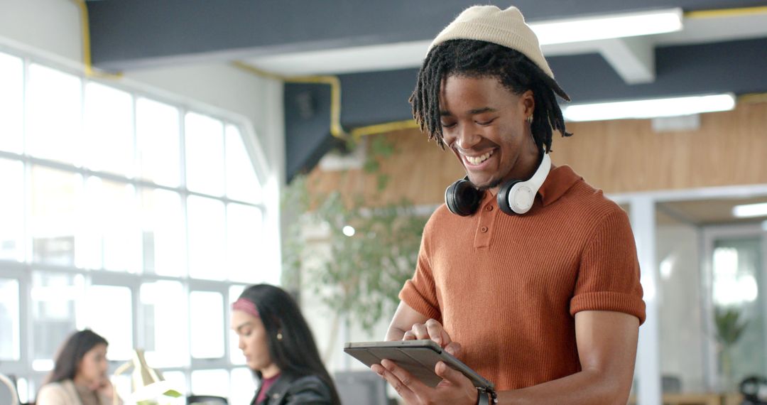 Young professional smiling and tapping tablet in bright coworking space with headphones