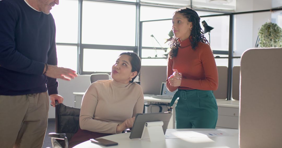 Multiracial team collaborating around tablet and documents in bright daylight office