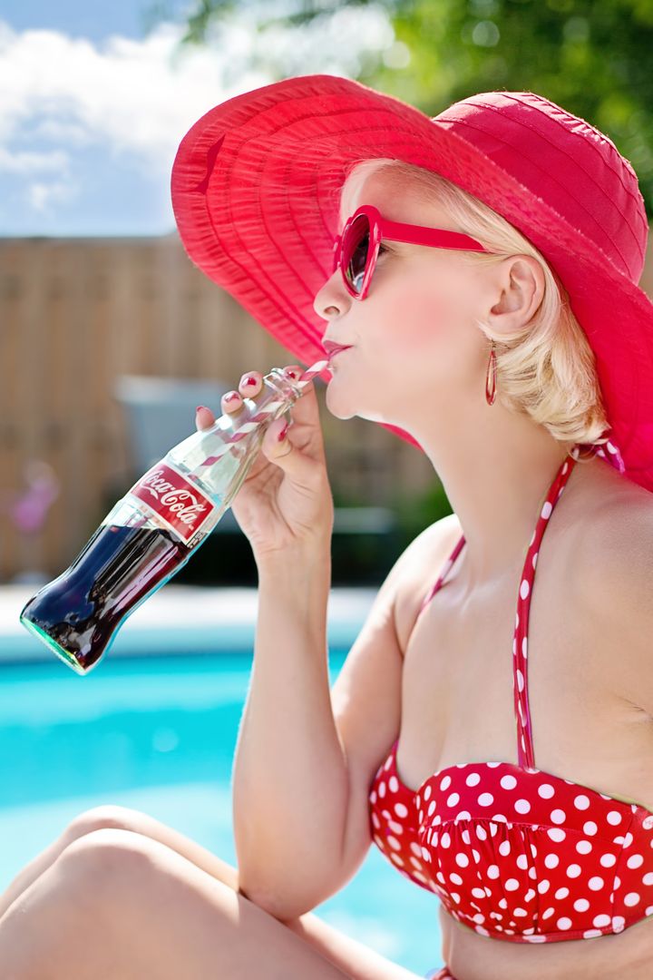 Woman in Red Polka Dot Print Bikini Wearing Red Frame Sunglasses Drinking Coca Cola Beverage in Blue and White Clouds - Free Images, Stock Photos and Pictures on Pikwizard.com