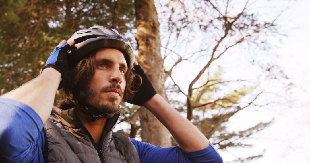 Man putting on bicycle helmet in forest during daytime - Free Images, Stock Photos and Pictures on Pikwizard.com