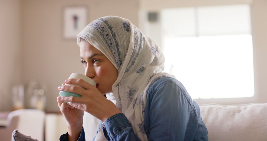 Young Woman in Headscarf Drinking Coffee in Relaxed Living Room Setting - Free Images, Stock Photos and Pictures on Pikwizard.com