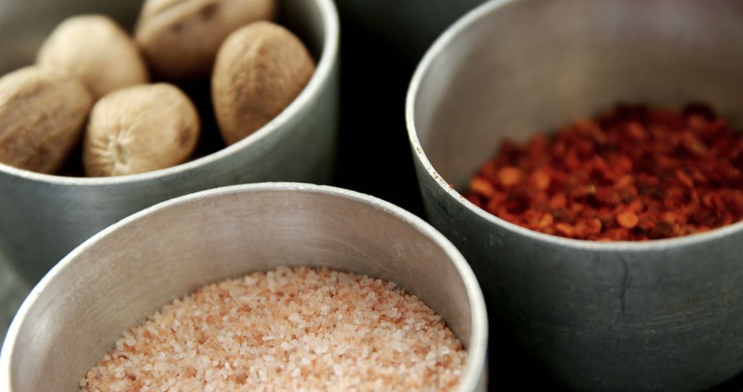 Three metal bowls hold nutmegs, pink salt, and red pepper flakes, key for flavorful dishes. - Free Images, Stock Photos and Pictures on Pikwizard.com